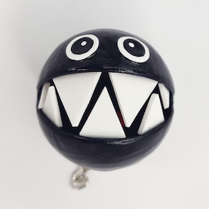 May include: Black and white 3D printed figurine of a character with a large mouth and sharp teeth. The character has two large white eyes and a black body.