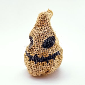 May include: A burlap sack with a black painted face, resembling a scary character. The face has two eyes and a wide, toothy grin.