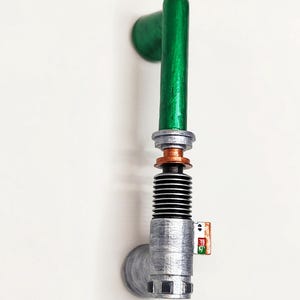 May include: A vertical wall-mounted handle featuring a metallic silver base and grip section with a copper-colored ring, topped by a smooth, cylindrical green handle. The silver section includes a small rectangular detail with red and green accents.