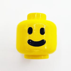 May include: A yellow plastic Lego head with a black smiling face and black eyes.