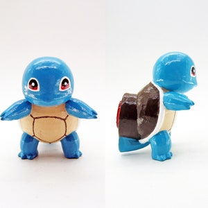 May include: A blue and brown hand-painted figurine of a turtle Pokemon. The turtle is standing on its four legs with its head up. The turtle has a brown shell with a red accent.