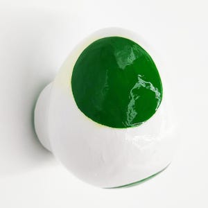 May include: White ceramic knob with a green circle painted on the top. The knob is round and has a smooth surface.