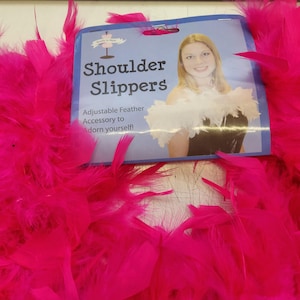 Könnte beinhalten: Leuchtend pinke Federboa mit einem Etikett mit der Aufschrift "Shoulder Slippers". Das Etikett besagt auch "Verstellbares Feder-Accessoire, um sich zu schmücken!" Ein auffälliges Accessoire.