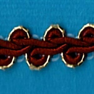 May include: A close-up of brown trim with gold accents. The trim is made of a woven fabric with a repeating pattern of circles.