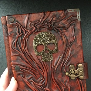 It features an embossed real leather cover with an old school style skull on it. Leather journal has swing hook clasp closure.