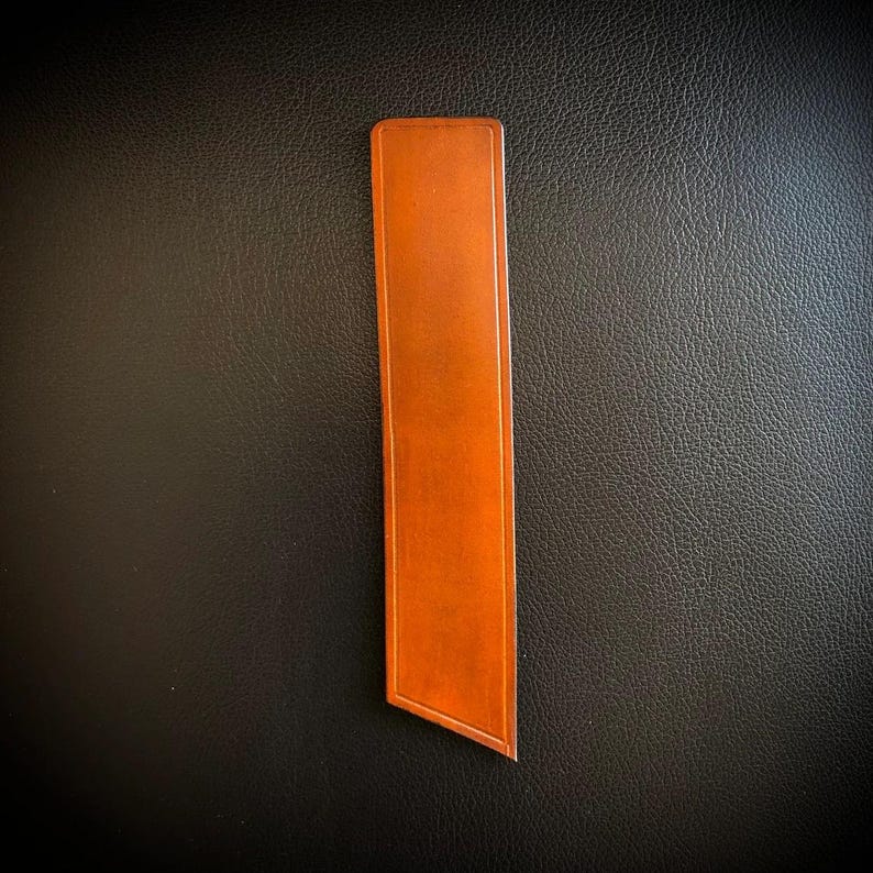 Handcrafted taba-colored leather bookmark with a diagonal pointed end, matching accessory for handmade leather journals.