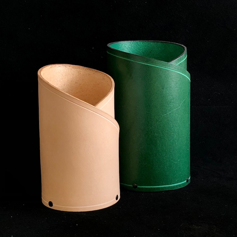 K&ouml;nnte beinhalten: Zwei Bleistifthalter aus Leder, einer ist beige und der andere gr&uuml;n. Beide haben eine gerollte Oberseite und sind zusammengen&auml;ht.