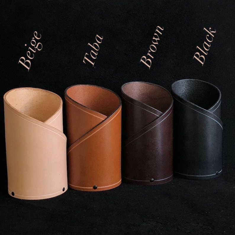 K&ouml;nnte beinhalten: Vier Lederarmb&auml;nder in verschiedenen Farben: Beige, Braun, Braun und Schwarz. Jedes Armband ist aufgerollt und hat eine gen&auml;hte Naht.