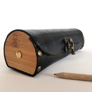 Puede incluir: Un estuche para lápices de cuero negro con un extremo de bambú y un cierre de latón. El estuche está hecho de materiales reciclados.