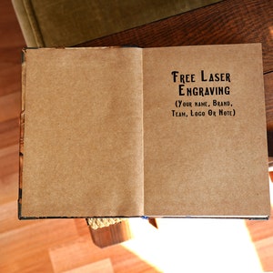 Open handmade leather journal showing engraved words on kraft paper first page, personalized gift option.