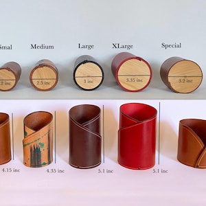 K&ouml;nnte beinhalten: Ein Set mit 10 Bleistifthaltern aus Leder in verschiedenen Gr&ouml;&szlig;en und Farben. Die Halter sind aus braunem, rotem und braunem Leder gefertigt und haben ein Kreuzmuster. Die Halter sind mit ihrer Gr&ouml;&szlig;e in Zoll gekennzeichnet: Klein (2,2 Zoll), Mittel (2,5 Zoll), Gro&szlig; (3 Zoll), XL (3,35 Zoll), Spezial (3,2 Zoll), 4,15 Zoll, 4,35 Zoll, 5,1 Zoll, 5,1 Zoll und 3,55 Zoll.