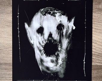 May include: A monochrome art print depicting a distorted face with a gaping mouth and sharp teeth. The image has a textured, ghostly appearance, with white highlights against a dark background. A white border with thorn-like details frames the artwork.