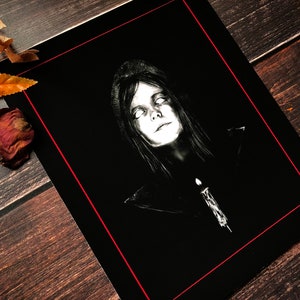 Puede incluir: Impresi&oacute;n art&iacute;stica en blanco y negro que presenta un retrato de una persona con cabello largo y ojos blancos brillantes. La obra de arte est&aacute; enmarcada con un borde rojo e incluye una vela. La imagen tiene un tema g&oacute;tico u horror.