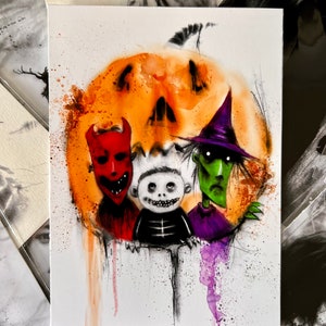 Pode incluir: Pintura em aquarela com três personagens assustadores em frente a uma abóbora laranja. Os personagens incluem um diabo vermelho, um esqueleto e uma bruxa verde. A obra de arte tem um tema de Halloween com respingos de tinta.