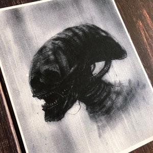 May include: A black and white drawing of an alien creature with a large head and sharp teeth. The creature is depicted in profile, with its head turned to the side. The drawing is done in a realistic style, with detailed shading and texture.