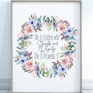 May include: A framed print featuring a watercolour floral wreath in shades of pink, blue, and grey. The wreath surrounds the text "She is clothed with Strength and Dignity She Is Proverbs 31".