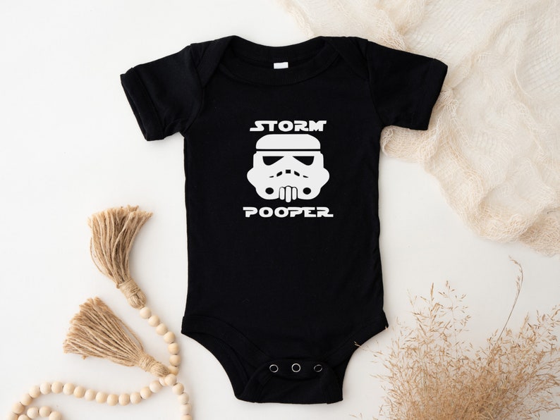baby star wars onesie. Black onesie with a  storm trooper head and the words storm pooper applied in white vinyl on the front.