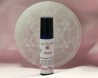 May include: A small blue glass bottle with a black rollerball top and a white label that reads "Gray Moon Goddess Shield" and "adds a layer of protection around your body. Made with Essential oils, jojoba oil & crystals."