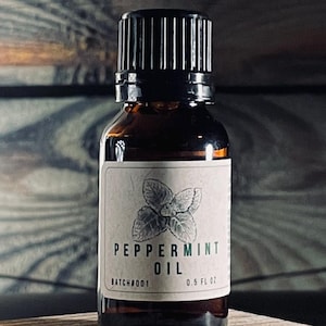May include: A small brown glass bottle with a black cap, containing peppermint oil. The bottle has a white label with the text "Peppermint Oil" and "BATCH#005 0.5 fl oz".