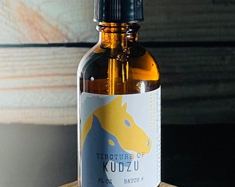 May include: A brown glass bottle with a black dropper top and a white label. The label has a blue and yellow illustration of a horse's head and the text "Tincture of Kudzu" and "1 fl oz Batch #".