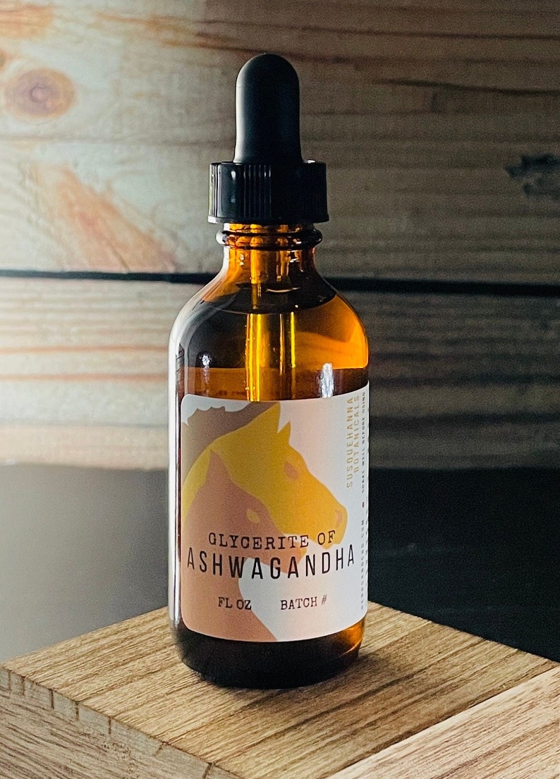 K&ouml;nnte beinhalten: Eine braune Glasflasche mit Tropfer, beschriftet mit "Glycerite of Ashwagandha" und "FL OZ BATCH #". Die Flasche steht auf einer Holzoberfl&auml;che.