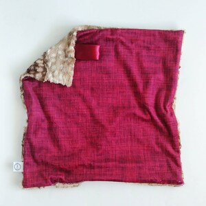 May include: A burgundy faux fur throw blanket with a brown faux fur trim. The blanket has a satin ribbon tied around it.