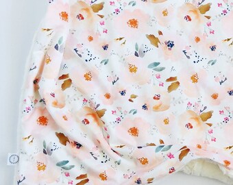 May include: A soft, white blanket with a delicate floral pattern in shades of pink, orange, and brown. The blanket is made of a lightweight fabric and has a fuzzy texture.