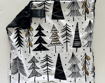 Puede incluir: Una manta para bebé con estampado en blanco y negro con un borde de piel sintética negra. El estampado presenta árboles estilizados en negro, blanco y dorado.