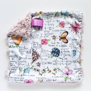 May include: A white fabric square with pink fuzzy trim features a hand-drawn illustration of mathematical equations and flowers. The equations include formulas for volume, area, and solid of revolution. The flowers are drawn in pink, red, and blue.