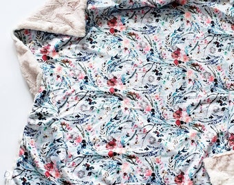 May include: A soft, plush blanket with a floral print on one side and a fluffy, white faux fur on the other side. The floral print features a variety of pink, blue, and green flowers on a white background.