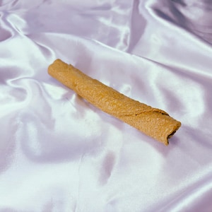 May include: A brown, rolled dog chew treat on a white satin background.
