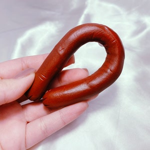 以下が含まれることがあります： ソーセージのような、茶色いゴム製のリング状の物が、手で持たれています
