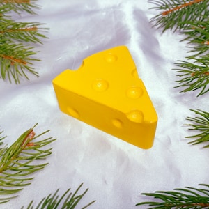 Puede incluir: Un adorno amarillo con forma de queso con una superficie texturizada y agujeros. El adorno está sobre un fondo blanco.