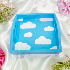May include: A blue wooden tray with white painted clouds. The tray has two handles on the sides.
