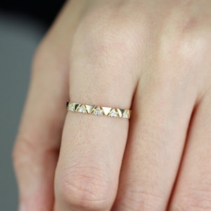 Pu&ograve; includere: Un anello color oro con un motivo ripetuto di triangoli e piccole gemme trasparenti. L'anello &egrave; indossato su un dito, mostrando il suo design delicato e la sua maestria artigianale. La fascia dell'anello &egrave; sottile ed elegante.