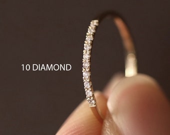 May include: A thin gold band with a row of 10 small diamonds set into the metal. The band is shown on a finger.