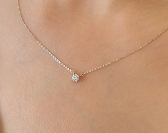May include: A delicate gold necklace featuring a small, round diamond pendant. The necklace has a thin chain and is worn around the neck. The diamond is the focal point, catching the light and adding a touch of sparkle.