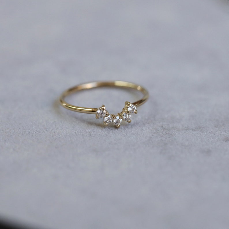 May include: A delicate gold band ring with a row of small, clear diamonds set in a curved arch shape.