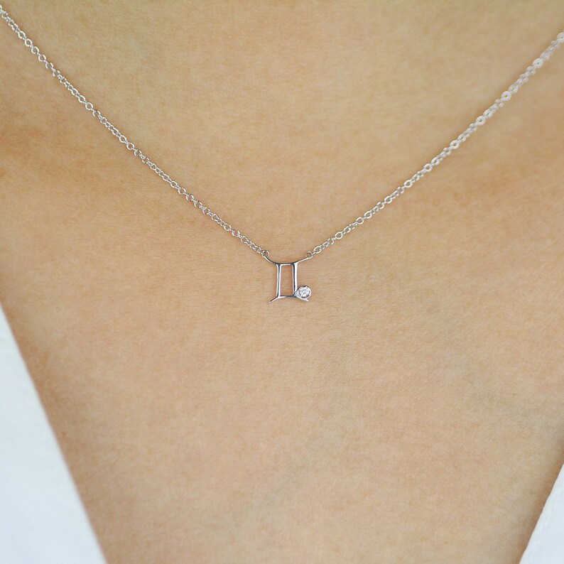 May include: A silver necklace with a Gemini zodiac symbol pendant and a small diamond accent.