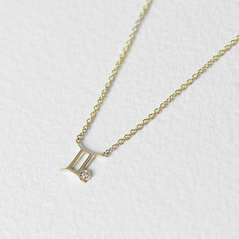 May include: A gold chain necklace with a Gemini zodiac symbol pendant featuring a small diamond accent.