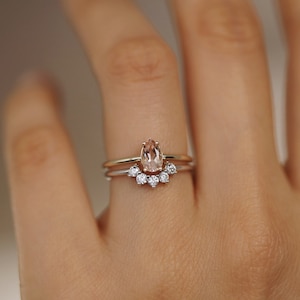 May include: A pear-shaped morganite gemstone ring set in a gold band, with a delicate band of smaller diamonds set in a crescent shape below the center stone.