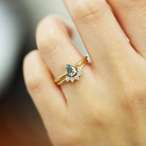May include: A gold ring set with a pear-shaped aquamarine gemstone and a band of smaller diamonds. The ring is worn on a finger.