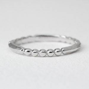 May include: A silver ring with a beaded design. The ring features a series of small, round beads set along the band, with faceted sections on either side. The ring is shown against a white background.