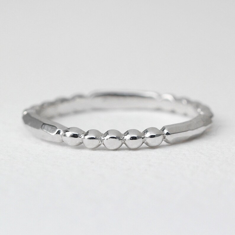 May include: A silver ring with a beaded design. The ring features a series of small, round beads set along the band, with faceted sections on either side. The ring is shown against a white background.