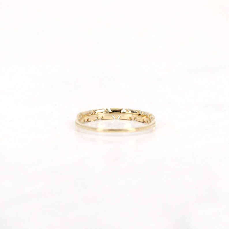 Pu&ograve; includere: Un delicato anello d'oro con un motivo geometrico ripetuto. L'anello presenta piccoli ritagli triangolari lungo la fascia, creando un motivo sottile e strutturato. L'anello &egrave; posto su uno sfondo bianco, evidenziando la sua finitura lucida.