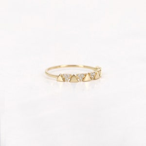 Pu&ograve; includere: Un delicato anello d'oro con una serie di piccole forme triangolari. Ogni triangolo &egrave; adornato da minuscole gemme scintillanti. L'anello ha una fascia sottile e una finitura lucida.