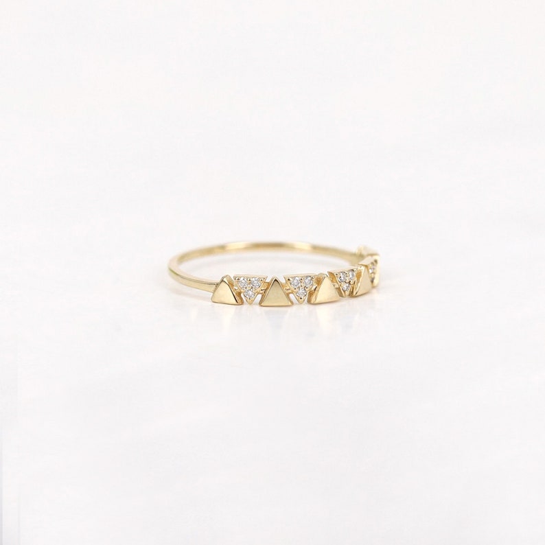 Pu&ograve; includere: Un delicato anello d'oro con una serie di piccole forme triangolari. Ogni triangolo &egrave; adornato da minuscole gemme scintillanti. L'anello ha una fascia sottile e una finitura lucida.