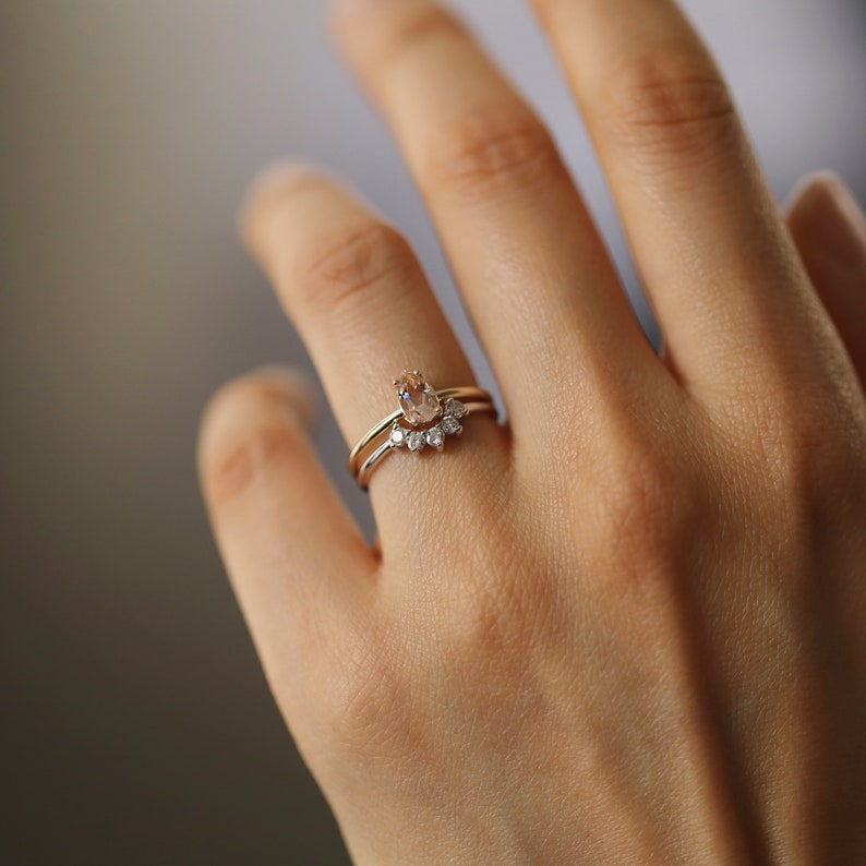 May include: A gold ring set with a pear-shaped gemstone and a band of smaller gemstones. The ring is worn on a person's finger.
