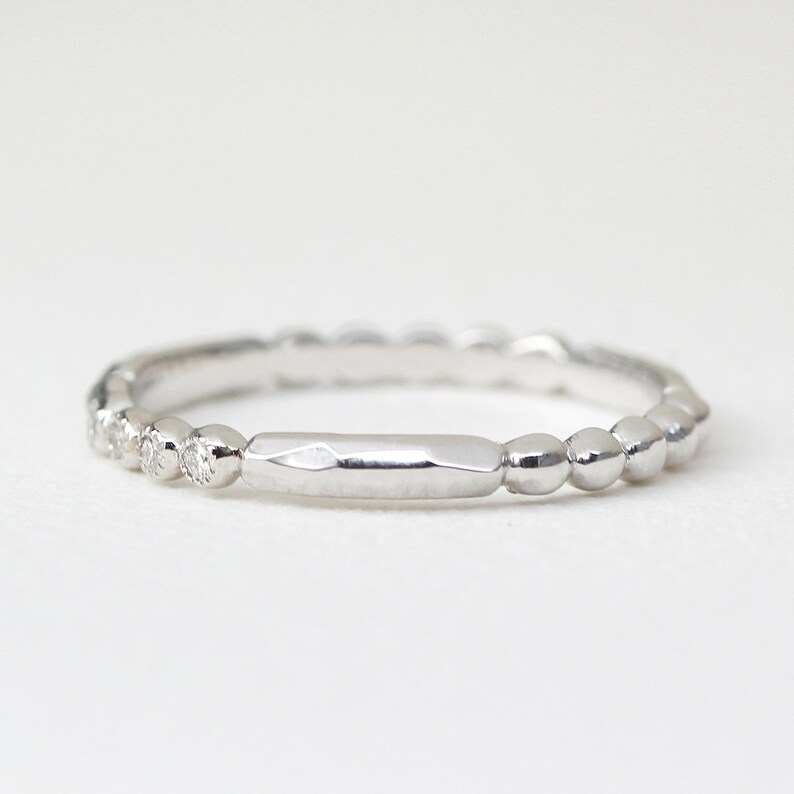 May include: A silver ring with a unique design. The ring features a series of small, round beads along the band, with a section of small diamonds and a flat, rectangular center. The ring is set against a white background.