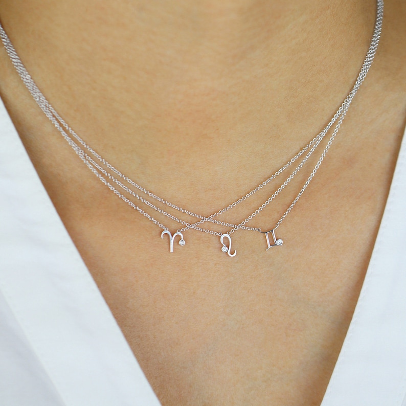 May include: Three delicate silver necklaces with zodiac symbols: Aries, Leo, and Gemini. Each pendant features a small diamond accent.